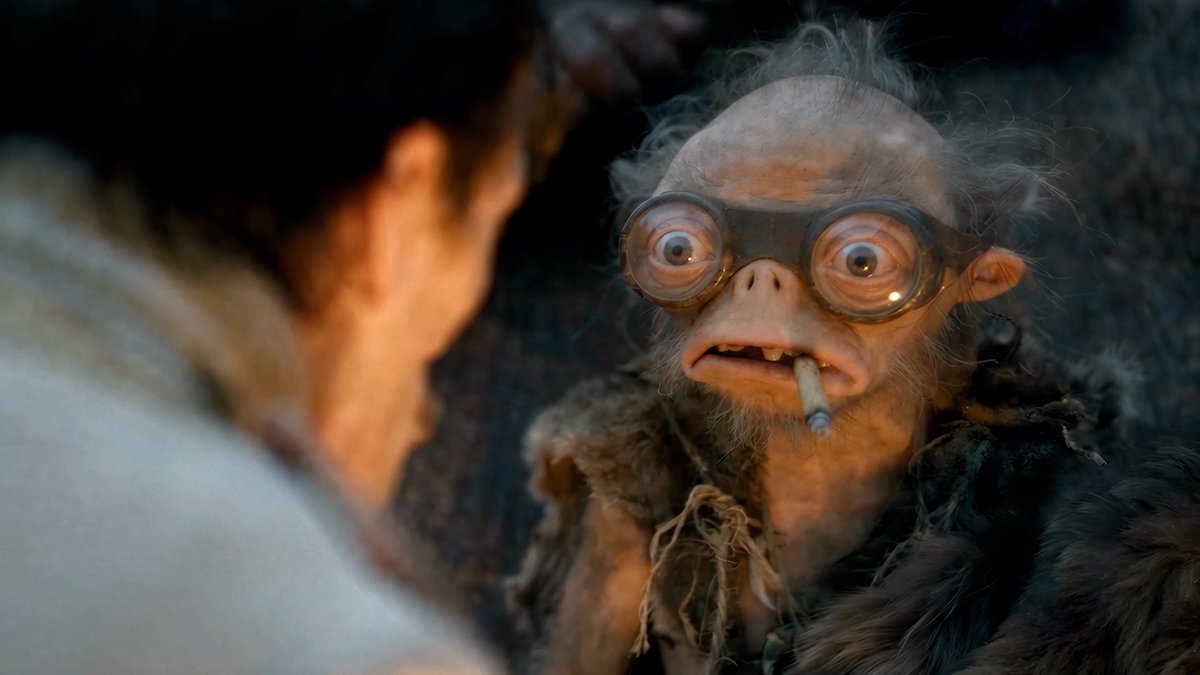 A goggled Bobo with a cigarette faces an out-of-focus person