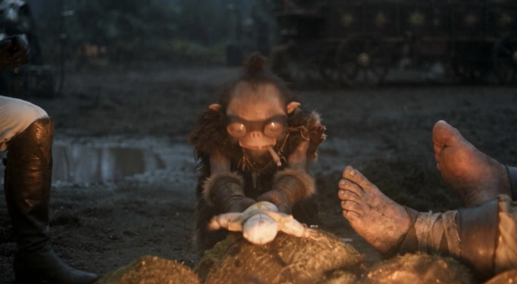 Goggled Bobo crouched at a mossy rock with a white doll between large bare feet